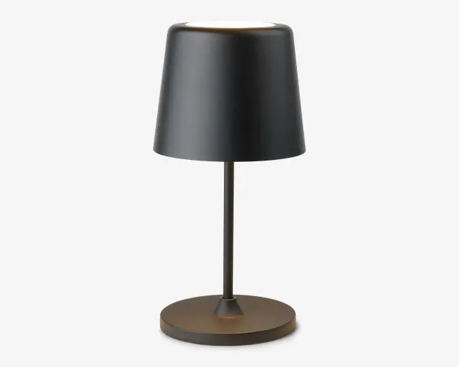 En moderne bordlampe med en mat sort, let konisk cylindrisk lampeskærm. Lampen har en slank, lige metalstang og en rund, flad fod i samme mørke finish. Designet er minimalistisk og stilrent, velegnet til moderne indretning.