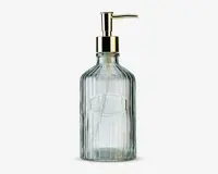 Dispenserflaske i klart glas med lodret rillet struktur, udstyret med en guldfarvet pumpe og et ovalt, hævet mærke på forsiden med ordet 'SOAP' præget. Flasken har et vintage-inspireret design og en solid bund.