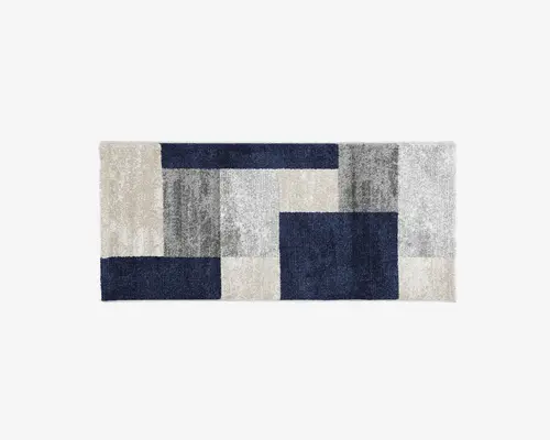 Rektangulært tæppe med et moderne geometrisk mønster bestående af store blokke i marineblå, lysegrå, mellemgrå og offwhite. Overfladen ser blød og luftig ud, og farveblokkene er arrangeret i et visuelt balanceret, abstrakt design.