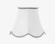 Hvid lampeskærm i stof med klokkeformet, udsvunget design. Nederste kant har en bølget afslutning med sølvfarvet kantbånd, og øverste kant er også afsluttet med sølvfarvet bånd. Stoffet er glat og let gennemsigtigt, hvilket giver en blød lysspredning.