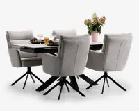 Et moderne spisebordssæt med et rektangulært bord med en glat, mørk bordplade og fire polstrede stole. Stolene er betrukket med lysegråt stof, har høje rygge, armlæn og står på sorte metalstel med fire ben og drejefunktion. Bordet er dækket med tallerkener, glas og en dekorativ vase med blomster, hvilket giver et indbydende og nutidigt udtryk.