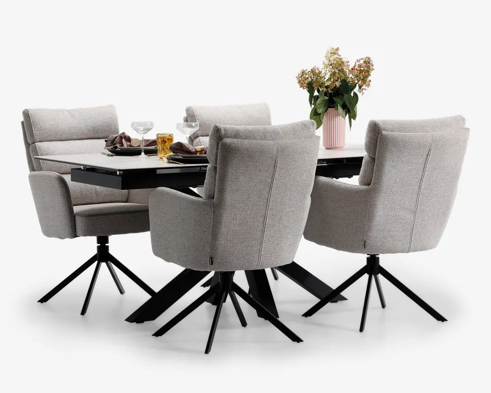 Et moderne spisebordssæt med et rektangulært bord med en glat, mørk bordplade og fire polstrede stole. Stolene er betrukket med lysegråt stof, har høje rygge, armlæn og står på sorte metalstel med fire ben og drejefunktion. Bordet er dækket med tallerkener, glas og en dekorativ vase med blomster, hvilket giver et indbydende og nutidigt udtryk.