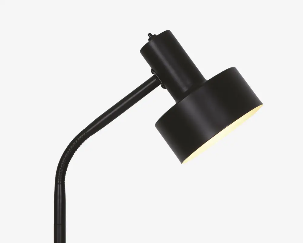 Nærbillede af lampens hoved med en mat sort cylindrisk skærm og en let vinklet hals. Lampen har et moderne, minimalistisk design med en glat overflade og en nedadrettet lysåbning.