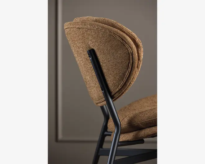 Nærbillede af en stol med polstring i brun, tekstureret stof på både sæde og ryglæn. Både sæde og ryglæn er tykt polstrede for ekstra komfort og har afrundede kanter samt et lagdelt udseende. Stellet er lavet af sort metal med mat finish, hvilket giver et moderne og robust udtryk.