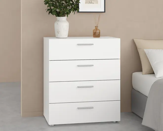 En moderne hvid kommode med fire rummelige skuffer, hver med et elegant sølvgreb. Kommoden har et minimalistisk design med rene linjer og en glat overflade. Den står på små, diskrete fødder og er dekoreret med en hvid keramisk vase med grønne blade samt en lille ravfarvet diffuserflaske på toppen.