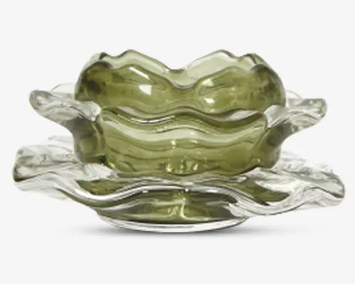 Dekorativ glasskål med bølget, kantskåret design. Skålen har en olivengrøn tone og står på en matchende klar glasunderkop, begge med organiske, bølgende former, der giver et moderne og kunstnerisk udtryk. Glasset er tykt og glat, hvilket reflekterer lyset elegant.