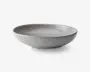 En rund, lav skål med en glat, mat lysegrå yderside og en blank inderside. Kanten er let forhøjet og har en diskret mørkere nuance, hvilket giver en elegant kontrast. Skålen har et minimalistisk, moderne design med rene linjer og en blødt buet form.