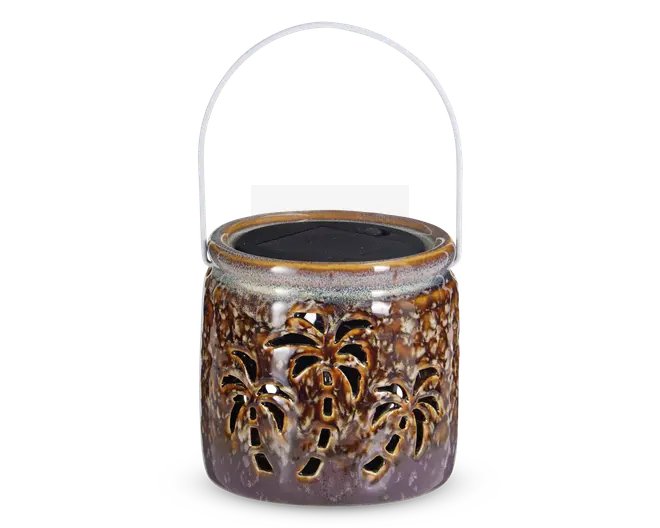 Dekorativ lanterne med blank, marmoreret brun og lilla keramisk overflade. Har udskårne palmetræ-designs rundt om siderne, så lyset kan skinne igennem. Lanternen er rund, har en bred åbning foroven og et metalhåndtag til ophængning. Toppen har en solcelle, hvilket indikerer, at den er solcelledrevet.