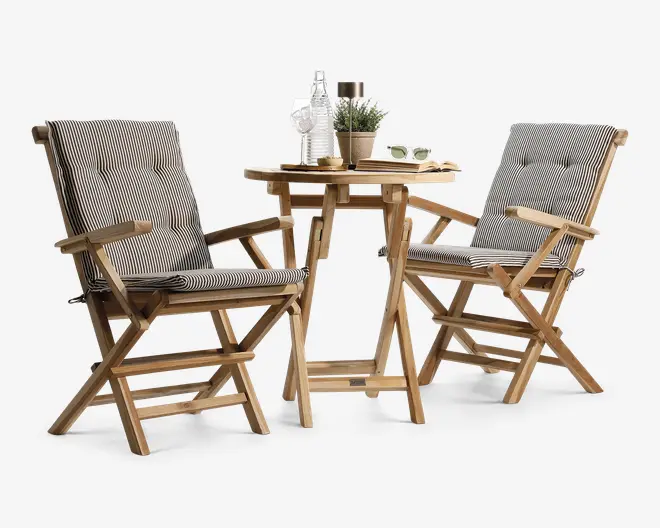 Sættet består af to træstole med armlæn og et rundt træbord. Stolene har tykke, polstrede hynder med sort-hvidt nålestribet mønster og knapdetaljer for ekstra komfort. Bordet har en hylde nederst til ekstra opbevaring eller dekoration. Træet har en naturlig finish, og designet er sammenklappeligt og egnet til både udendørs og indendørs brug. Tilbehør på bordet, såsom glas, plante og karaffel, er kun til udstillingsformål.