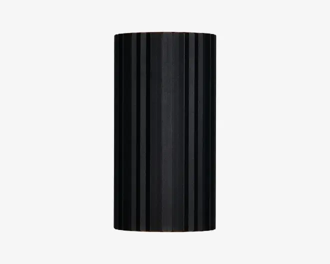 Høj, cylindrisk genstand med mat sort overflade og lodrette riller jævnt fordelt rundt om hele overfladen. Designet er stilrent og moderne med en ensartet tekstur, der både giver et interessant udseende og et skridsikkert greb. Top og bund er flade, og det samlede udtryk er minimalistisk.