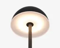 Nærbillede af en lampe med en bred, kuppelformet skærm. Lampens yderside er mat sort, mens indersiden er hvid og reflekterer et varmt, diffust lys. Lampestangen er metal med en mørk, struktureret overflade, og designet er moderne og minimalistisk.