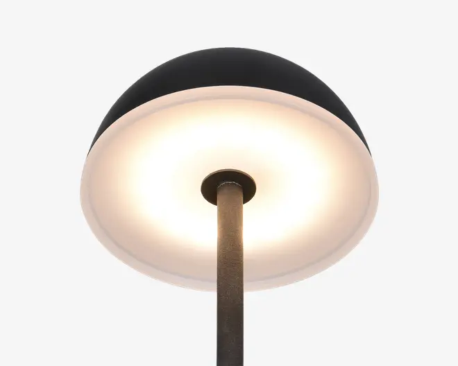 Nærbillede af en lampe med en bred, kuppelformet skærm. Lampens yderside er mat sort, mens indersiden er hvid og reflekterer et varmt, diffust lys. Lampestangen er metal med en mørk, struktureret overflade, og designet er moderne og minimalistisk.