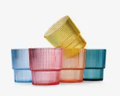 Sæt med seks lave, brede drikkeglas i forskellige gennemsigtige farver: lyseblå, pink, gul, orange og turkis. Hvert glas har en lodret rillet struktur på ydersiden, hvilket giver dem et moderne og stilfuldt udseende. Glassene kan stables og har en tyk, solid bund.