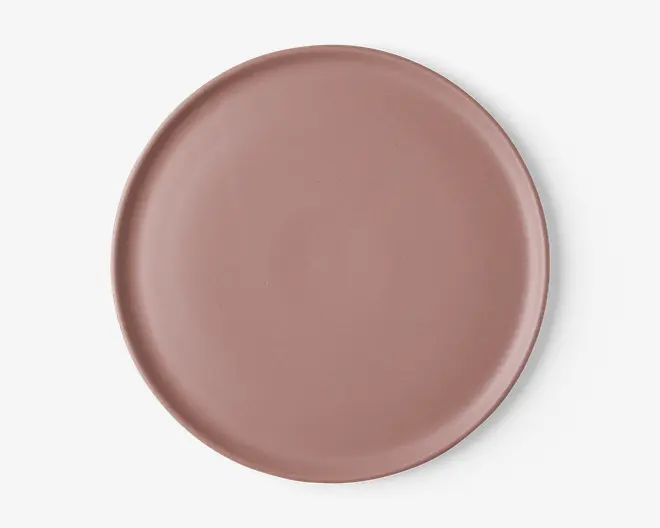 En rund, flad tallerken med en glat, mat overflade i en afdæmpet støvet rosa farve. Tallerkenen har en let hævet kant og et minimalistisk, moderne design uden mønstre eller dekorationer.