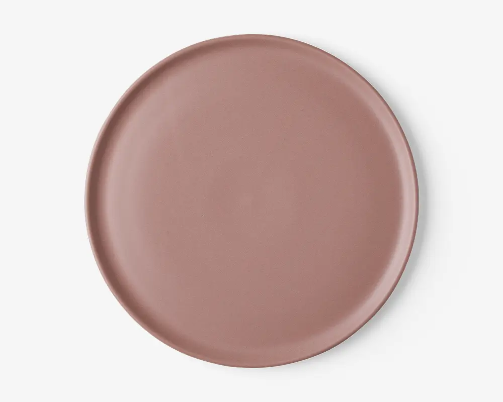 En rund, flad tallerken med en glat, mat overflade i en afdæmpet støvet rosa farve. Tallerkenen har en let hævet kant og et minimalistisk, moderne design uden mønstre eller dekorationer.