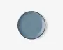 Rund keramiktallerken med en glat, blank overflade i en afdæmpet blå farve. Tallerkenen har en let hævet kant og et minimalistisk, moderne design uden mønstre eller dekorationer.