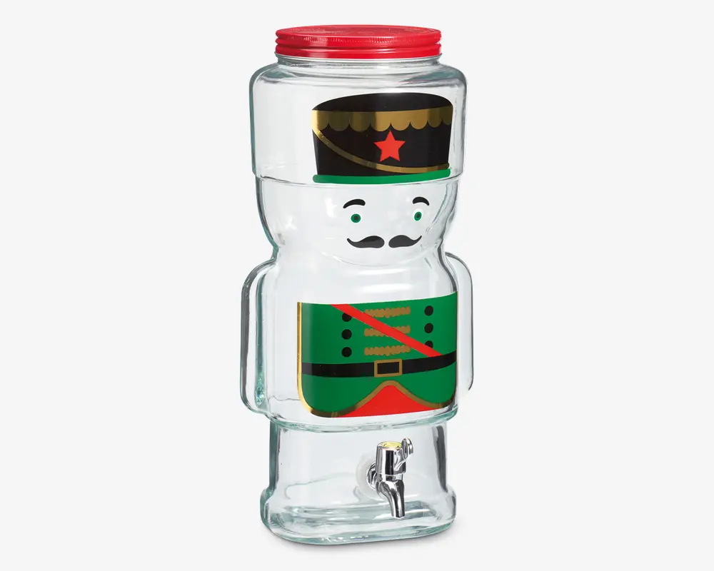 Gennemsigtig glasdrikkedispenser formet som en tinsoldat, med et trykt design der viser en grøn uniform, rød skråbånd, sort bælte og sort hat med gul kant og rød stjerne. Dispenseren har et rødt skruelåg øverst og en sølvfarvet tappehane nederst for nem udskænkning.