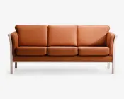 En tresæders sofa med glat, lysebrunt læderbetræk og bløde, aftagelige sæde- og ryghynder. Sofaen har en lys træramme med let buede armlæn og ben, hvilket giver et moderne og minimalistisk udtryk. Hynderne er tykke og jævnt fordelt, hvilket giver behagelig siddeplads til tre personer.