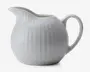 En hvid keramisk kande med blank overflade, rund form og diskret lodret rillet struktur. Den har en bred tud for nem hældning og et stort, buet håndtag for komfortabelt greb.