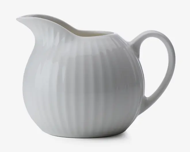 En hvid keramisk kande med blank overflade, rund form og diskret lodret rillet struktur. Den har en bred tud for nem hældning og et stort, buet håndtag for komfortabelt greb.