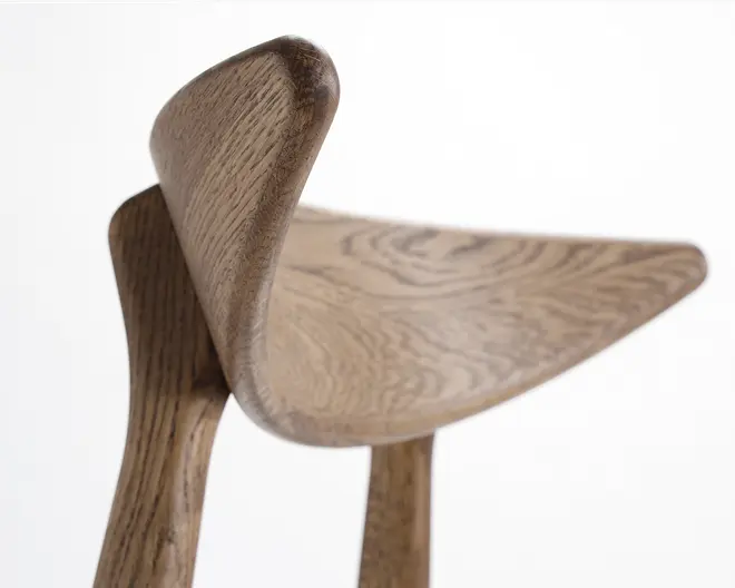 Nærbillede af et træsæde med glat, buet ryglæn og sædeflade. Træets årer er tydelige og har en naturlig finish. Kanterne er afrundede for komfort, og håndværket fremhæver sømløse samlinger og et minimalistisk, moderne design.