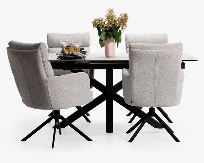 Sæt med fire moderne spisebordsstole betrukket med lysegråt stof, med høje rygge, polstrede sæder og armlæn for ekstra komfort. Hver stol har en sort metal-dreje-fod med fire skrå ben. Stolene er placeret omkring et rektangulært spisebord med hvid bordplade og sorte metalben. Bordet er pyntet med en lyserød vase med blomster, to vinglas og en tallerken med snacks.