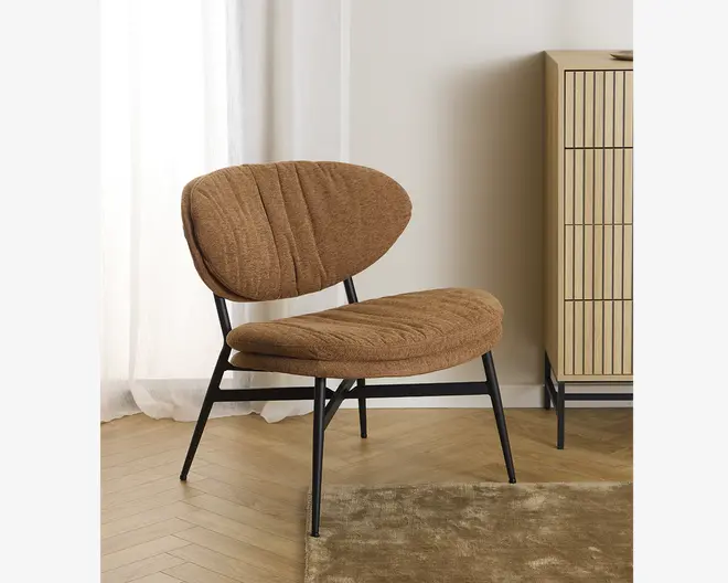 En moderne lænestol med buet, bred ryglæn og rummeligt sæde, begge polstret med tekstureret brunt stof. Stolen har diskrete lodrette syninger på puderne for ekstra detaljer. Den står på en slank, sort metalramme med skråtstillede ben, hvilket giver et moderne og robust udtryk.