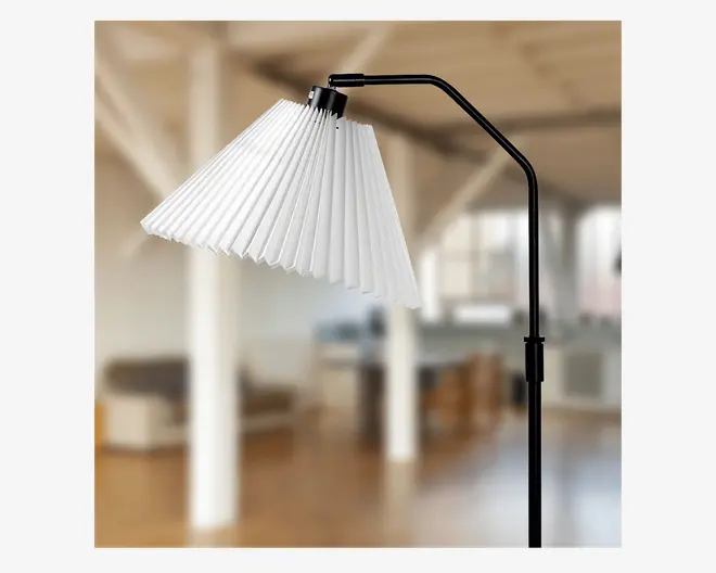 Moderne gulvlampe med sort metalstel og en vinklet arm. Lampeskærmen er hvid og plisseret, hvilket giver et vifteformet udtryk. Skærmen er monteret i en vinkel, hvilket giver lampen et moderne og kunstnerisk udseende. Lampens højde kan justeres, og designet er minimalistisk og stilfuldt.