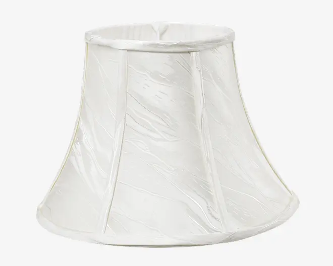 En klokkeformet lampeskærm lavet af hvidt stof med et diskret tekstureret mønster. Skærmen har lodrette sømme, der deler den i paneler, og en let udvidet bundkant. Top- og bundkanterne er afsluttet med en glat stofkant.