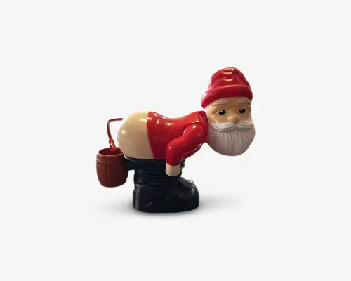 En sjov figur formet som en nisse, der bukker sig forover med bukserne trukket ned, så bagdelen er synlig. Nissen har en rød trøje, rød hue og sorte støvler på og holder en lille brun spand i den ene hånd. Designet er humoristisk og beregnet som en sjov dekoration til have eller hjem.