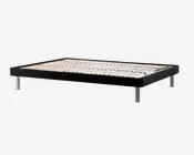 Lavt sengebund med en solid sort rektangulær ramme og jævnt fordelte lyse trælister til støtte af madrassen. Bunden står på seks cylindriske metalben med blank kromfinish, hvilket giver stabilitet og et moderne udtryk. Designet er minimalistisk og passer til moderne indretning.