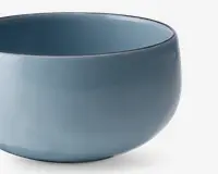 Rund keramikskål med en glat, blank overflade i en afdæmpet blå farve. Skålen har et enkelt, minimalistisk design med blødt buede sider og en bred åbning. Indersiden og ydersiden har samme farve, og kanten er let afrundet for komfort.
