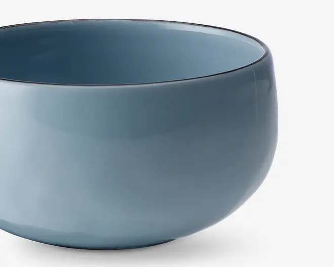 Rund keramikskål med en glat, blank overflade i en afdæmpet blå farve. Skålen har et enkelt, minimalistisk design med blødt buede sider og en bred åbning. Indersiden og ydersiden har samme farve, og kanten er let afrundet for komfort.