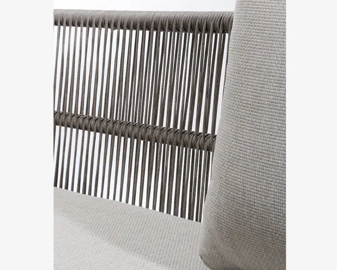 Nærbillede af et møbel med ryglæn bestående af tætsiddende lodrette reb i mørkegrå, som er vævet vandret to steder for ekstra stabilitet. Sædet og puden er betrukket med et lysegråt, tekstureret stof, der giver et blødt og komfortabelt udtryk.