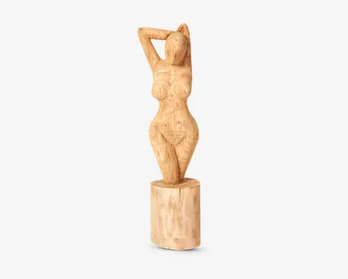 Håndskåret træskulptur, der forestiller en stiliseret kvindefigur med fremhævede kurver og et ansigtsløst hoved. Figuren står på en cylindrisk træfod med armene løftet og hænderne placeret bag hovedet. Overfladen har en rå, tekstureret finish, som fremhæver træets naturlige årer og farvevariationer.