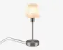 Lampen har en cylindrisk fod og stang i børstet metal, hvilket giver et moderne og stilrent udtryk. Lampeskærmen er lavet af et gennemsigtigt, mat materiale med et diskret marmoreret mønster, som spreder lyset blødt. Lampen har en synlig ledning, der går ud fra bunden, og egner sig godt til skriveborde eller sengeborde.