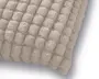 Nærbillede af blødt beige plysstof med et hævet, tufted firkantmønster og en afrundet, syet kant.
