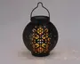 Rund sort lanterne med indviklede udskæringer, der lader varmt gult lys skinne igennem og skaber dekorative lysmønstre på omgivelserne. Lanternen har et håndtag øverst til nem transport eller ophængning samt en flad top, der muligvis rummer et solpanel til udendørs brug.