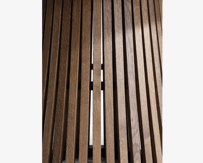 Nærbillede af lodrette trælister med jævn afstand og en glat, poleret overflade. Træet har en varm, mellembrun farve med synlige åretegninger, og listerne er adskilt af smalle mellemrum, der lader lys slippe igennem. Overfladen fremstår solid og veludført, velegnet til moderne eller minimalistiske indretninger.
