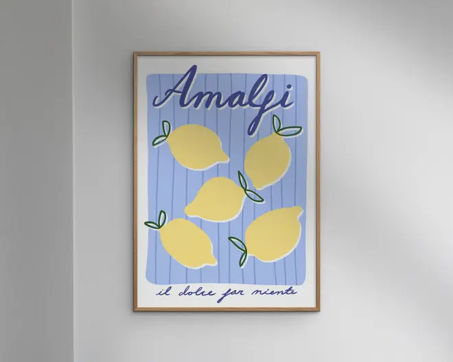 Indrammet kunsttryk med en legende illustration af fem gule citroner med grønne blade på en blå og hvidstribet baggrund. Øverst står ordet 'Amalfi' med store, blå, kursiverede bogstaver, og nederst ses sætningen 'il dolce far niente' med mindre håndskrift. Stilen er moderne og minimalistisk med en glad og sommerlig stemning.