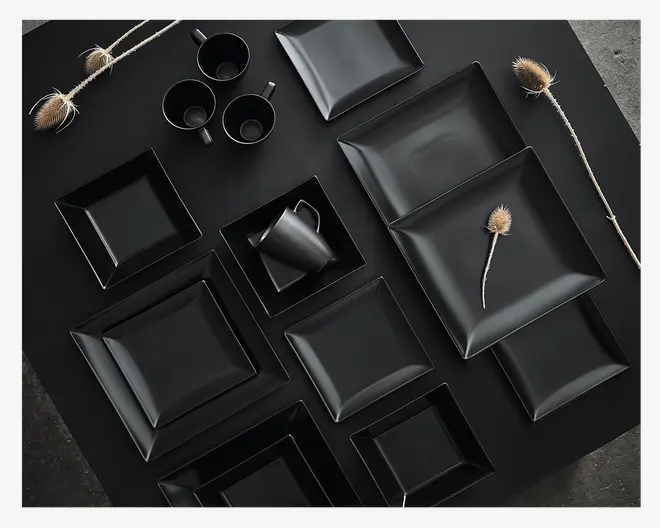 Et sæt mat sort service bestående af firkantede og rektangulære tallerkener og skåle i forskellige størrelser samt matchende krus. Delene har rene, moderne linjer og en glat, ikke-reflekterende overflade. Opstillingen fremhæver de geometriske former og det minimalistiske design, der passer til et moderne spisebord.