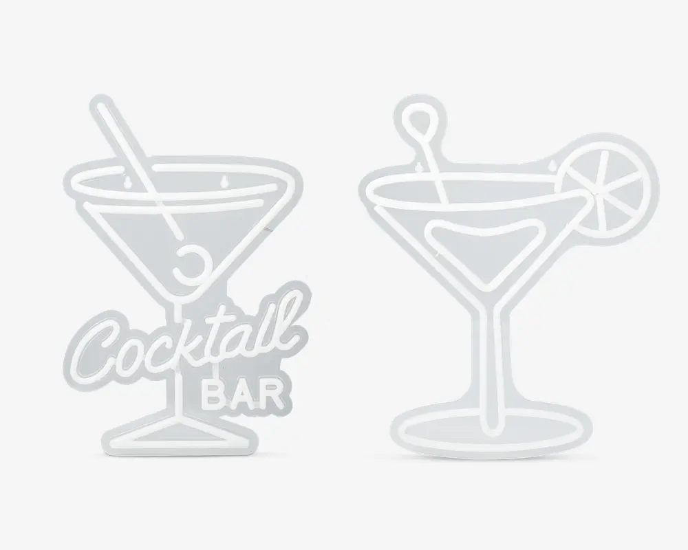 Sæt med to skilte i neon-stil formet som cocktailglas. Det ene skilt viser et martiniglas med en rørepind og en oliven samt teksten 'Cocktail Bar' i kursiv og blokbogstaver ved foden. Det andet skilt forestiller et lignende glas med en rørepind og en citron- eller limeskive på kanten. Begge skilte har en hvid kontur og er designet til at ligne lysende neonlys.