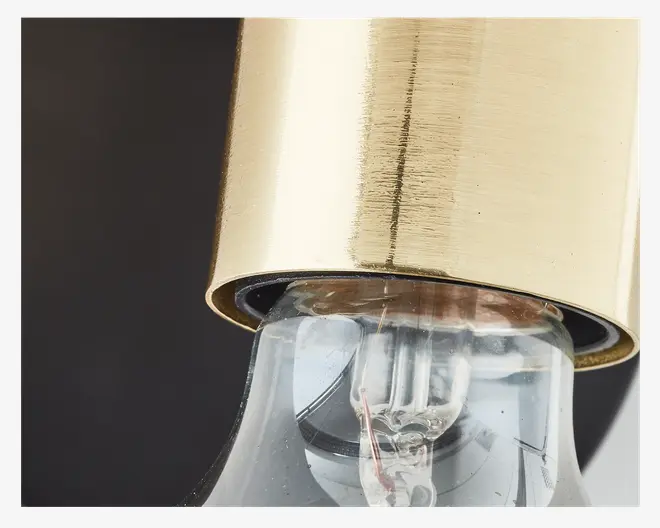 Nærbillede af en fatning med børstet gylden metalfinish. Fatningen holder en klar glaspære, hvor glødetråden og den indvendige ledning er synlig. Den gyldne overflade har en let tekstur, og pæren sidder sikkert fast i fatningen.