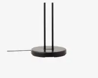 Nærbillede af en mat sort, cirkulær fod med to lodrette stænger, der går opad. Basen er flad og solid, og der går en ledning ud fra siden, hvilket antyder, at det er en elektrisk enhed. Designet er moderne og minimalistisk.