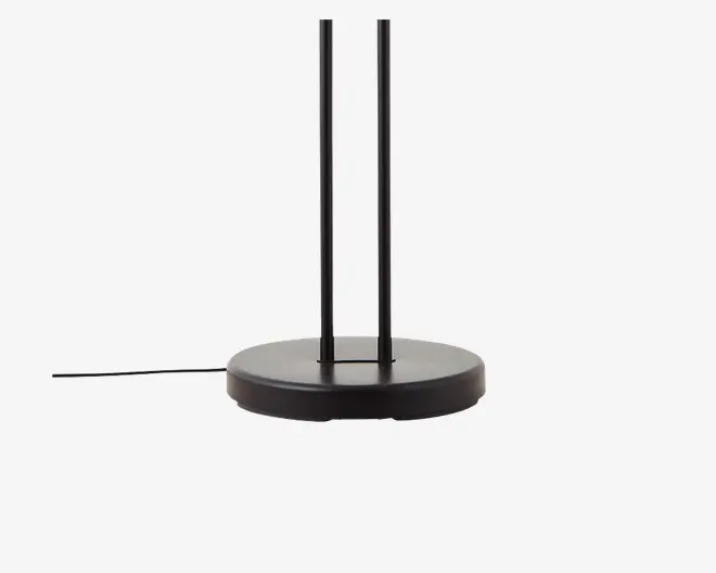 Nærbillede af en mat sort, cirkulær fod med to lodrette stænger, der går opad. Basen er flad og solid, og der går en ledning ud fra siden, hvilket antyder, at det er en elektrisk enhed. Designet er moderne og minimalistisk.