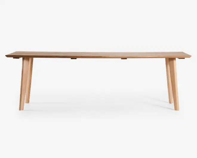 Rektangulær bænk lavet af lyst træ med en glat, flad overflade og fire skråtstillede ben for stabilitet. Designet er minimalistisk og moderne med rene linjer og en naturlig træstruktur.