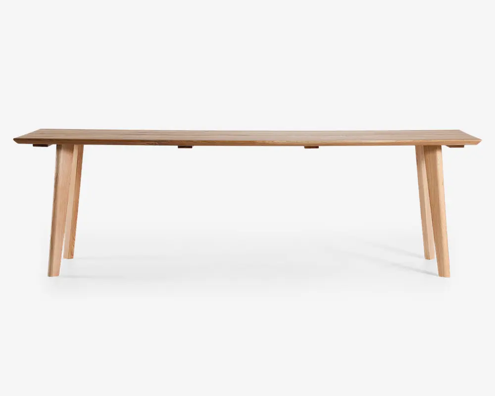 Rektangulær bænk lavet af lyst træ med en glat, flad overflade og fire skråtstillede ben for stabilitet. Designet er minimalistisk og moderne med rene linjer og en naturlig træstruktur.