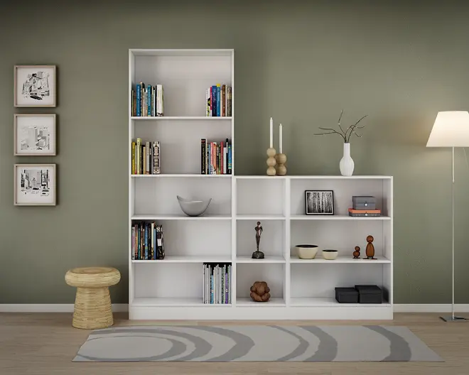 Moderne hvid reol med både høje og lave sektioner og åbne hylder. Hylderne er dekoreret med bøger, dekorative skåle, vaser, lys, små skulpturer, indrammede fotos og opbevaringskasser. Reolen står op ad en afdæmpet grøn væg, på et lyst trægulv med et moderne tæppe i grå nuancer. Udtrykket er minimalistisk og organiseret, velegnet til stue eller kontor.