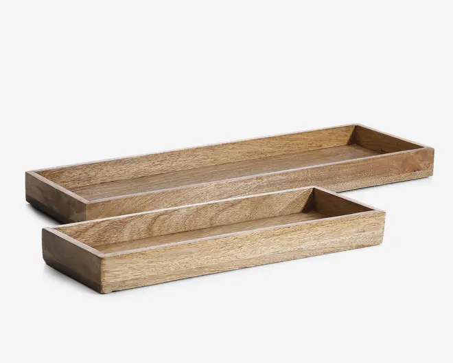 Sæt med to rektangulære bakker i lyst træ med synlig træstruktur. Begge bakker har lige, glatte sider og en flad bund. Bakkerne er lave og findes i to forskellige størrelser, hvor den ene er større og længere end den anden. Det enkle og minimalistiske design gør dem velegnede til organisering eller fremvisning af genstande.