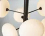 Nærbillede af en moderne lampe med flere matterede glasglober, der er fastgjort til en central sort metalstang med tynde sorte arme. Globerne udsender et blødt, varmt lys, og designet har et moderne, geometrisk udtryk.